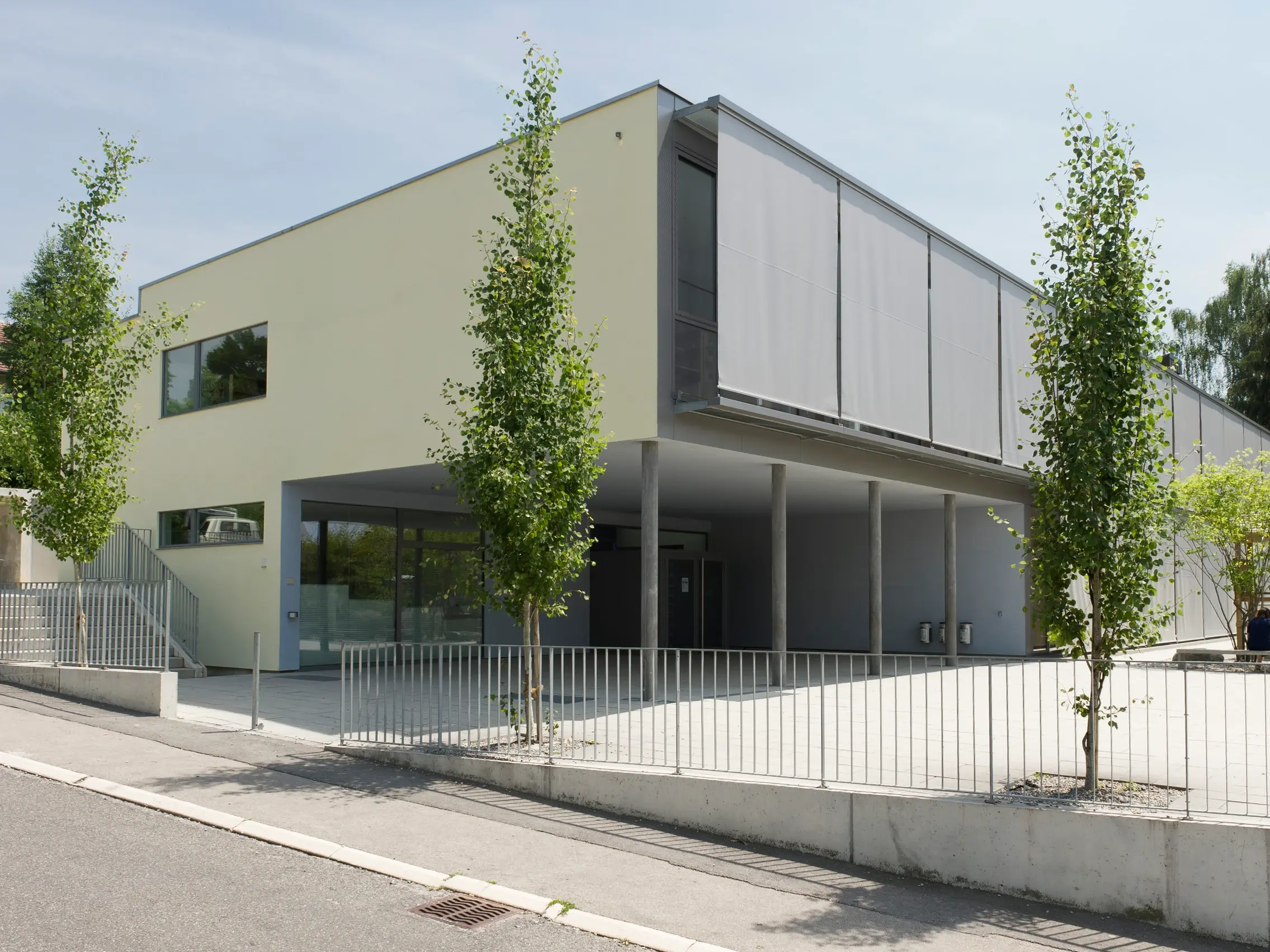 Bâtiment scolaire avec colonnes et ombrage de façade, crépi vert clair