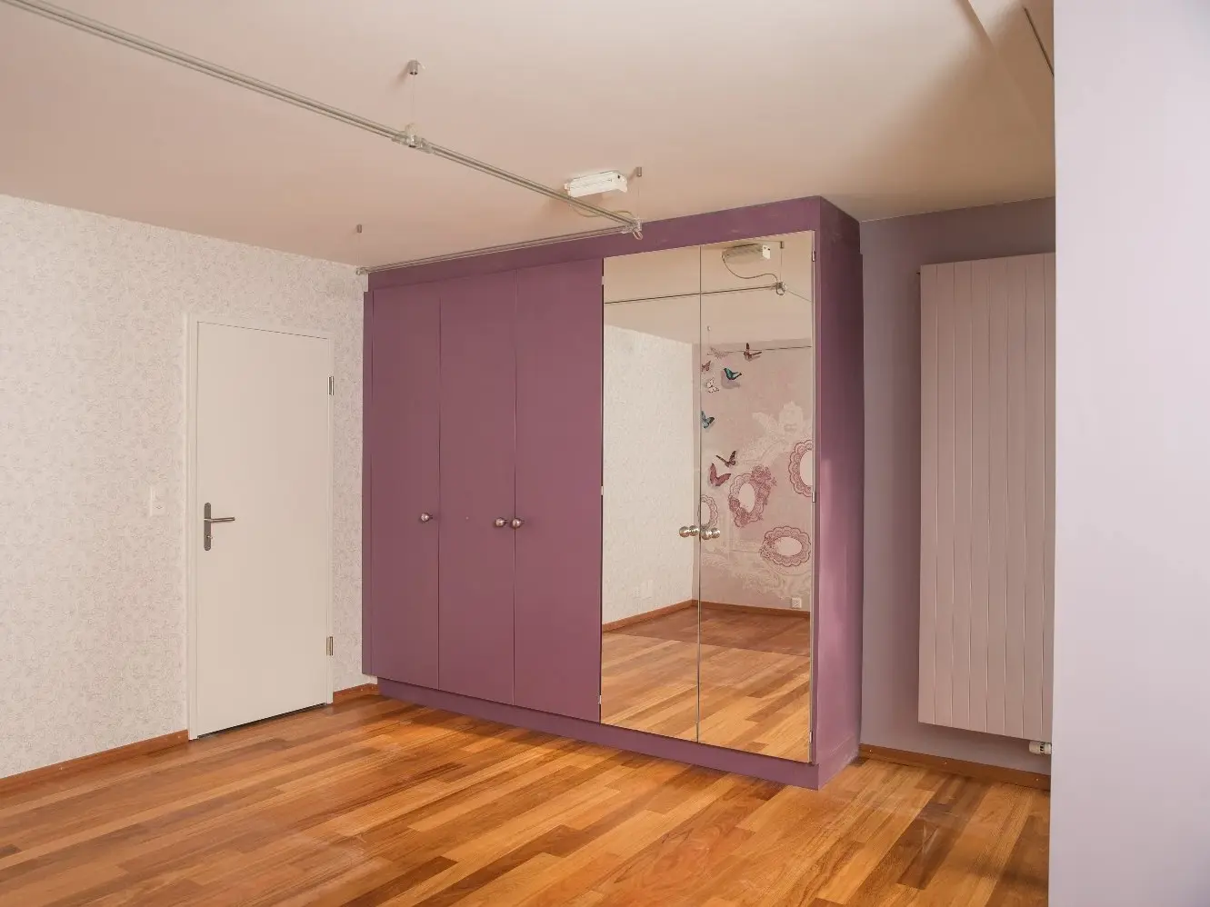 Murs intérieurs blancs, parquet et une armoire encastrée de couleur violette avec une grande surface miroir