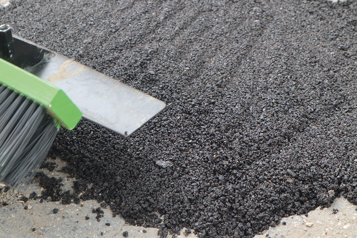 Der Kaltasphalt wird auf den Boden plattgeklopft