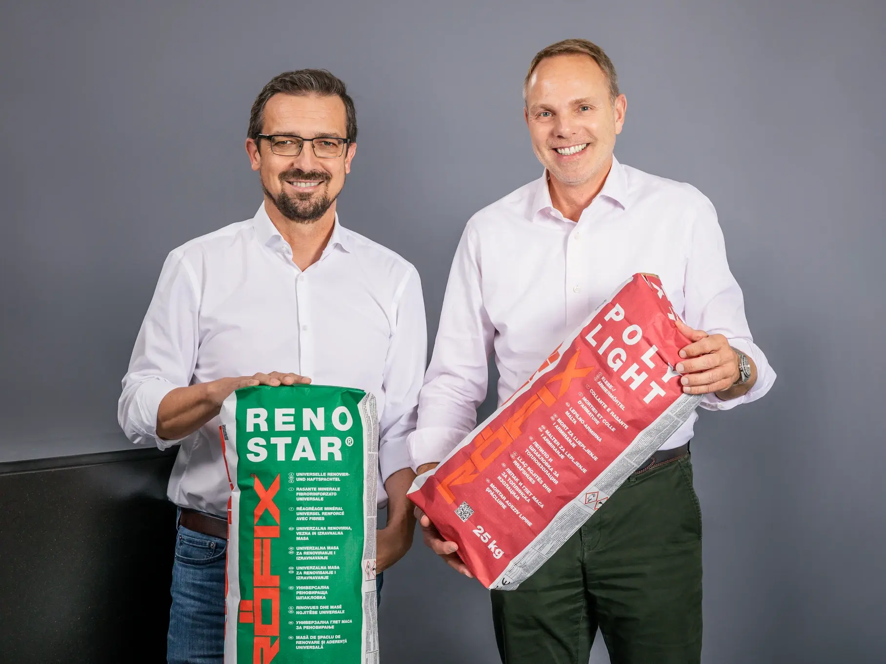 Deux hommes en chemise blanche tenant deux sacs d'emballage Röfix avec des inscriptions vertes et rouges