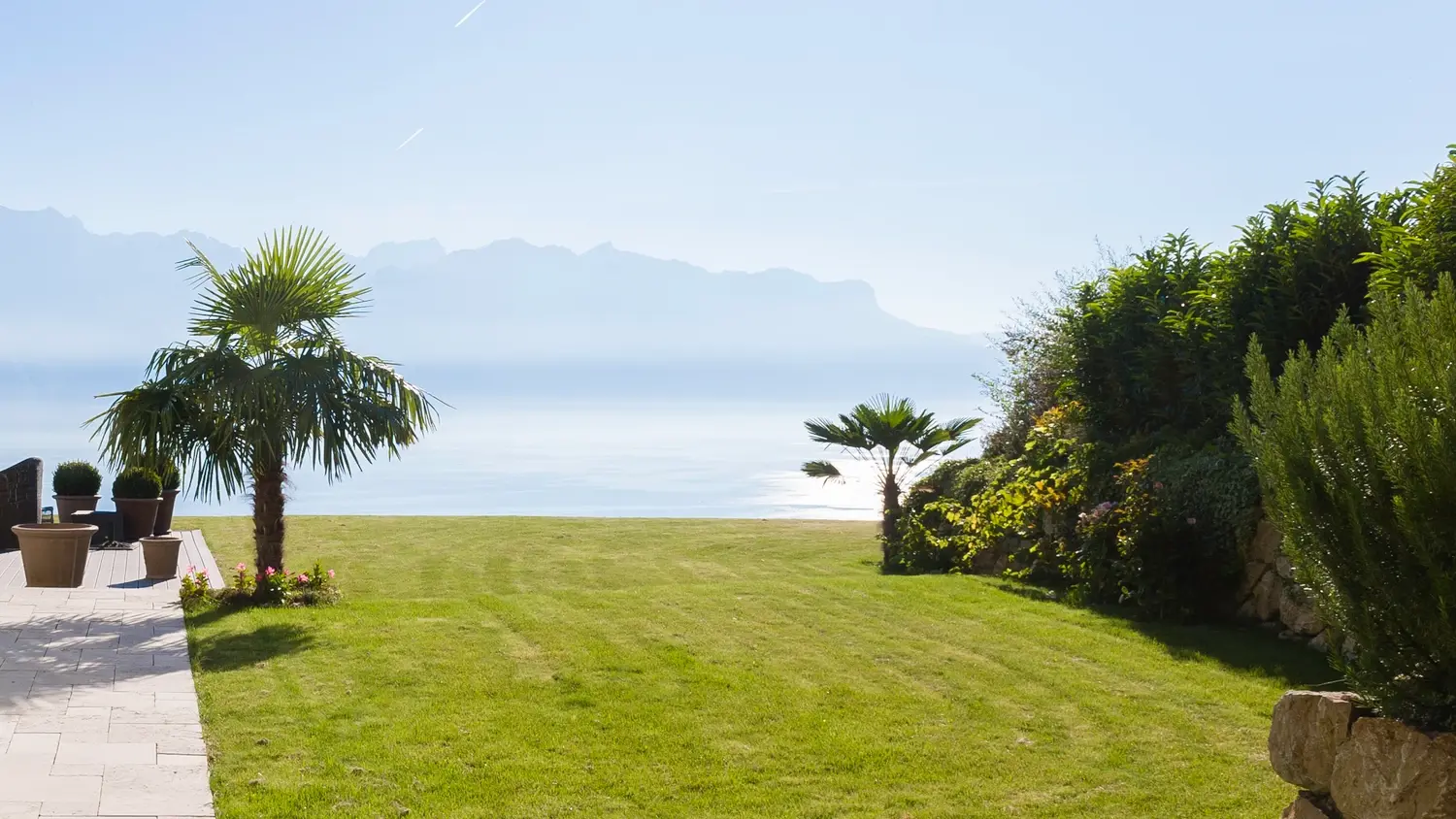 Jardin avec pelouse à l'anglaise, palmier, lac et panorama montagneux