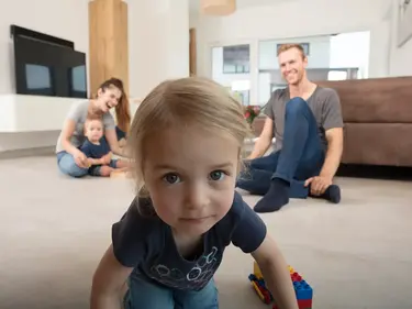 Das Kind schaut nah in die Kamera, die Eltern sind im Hintergrund 