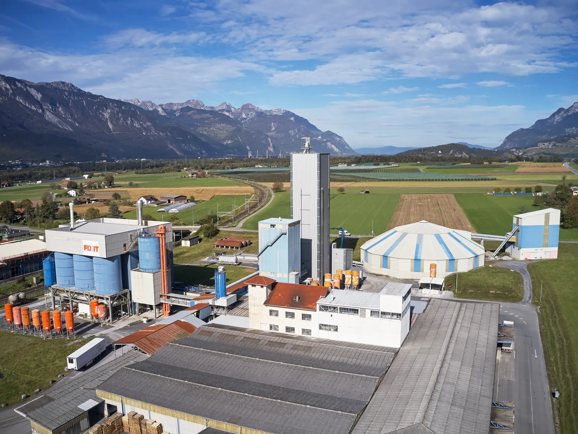Luftaufnahme des Produktionswerks der Fixit AG in Bex mit Steinhalle, Lagerbereichen und Fixit Silos