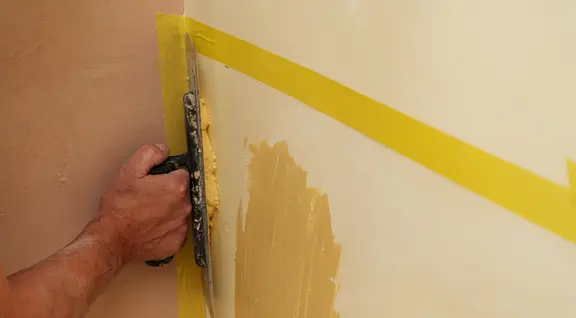 Hand mit Kelle verputzt die Wand 