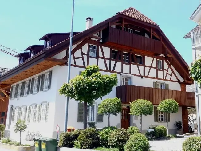 Gebäude mit Fachwerk im Dachfirst-Bereich und davor kugelförmige Bäume und Büsche zur Begrünung