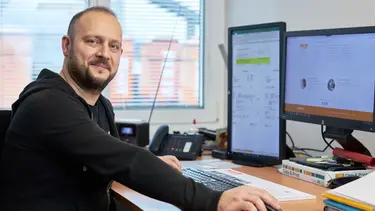 L'employé de Fixit sourit à la caméra, il est assis à son bureau devant deux écrans