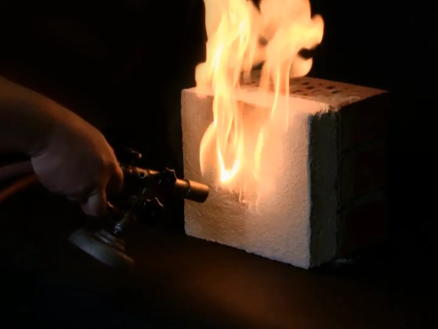 Un bec Bunsen est dirigé vers l'enduit isolant Fixit 222 Aerogel, produisant des flammes jaunes ardentes.