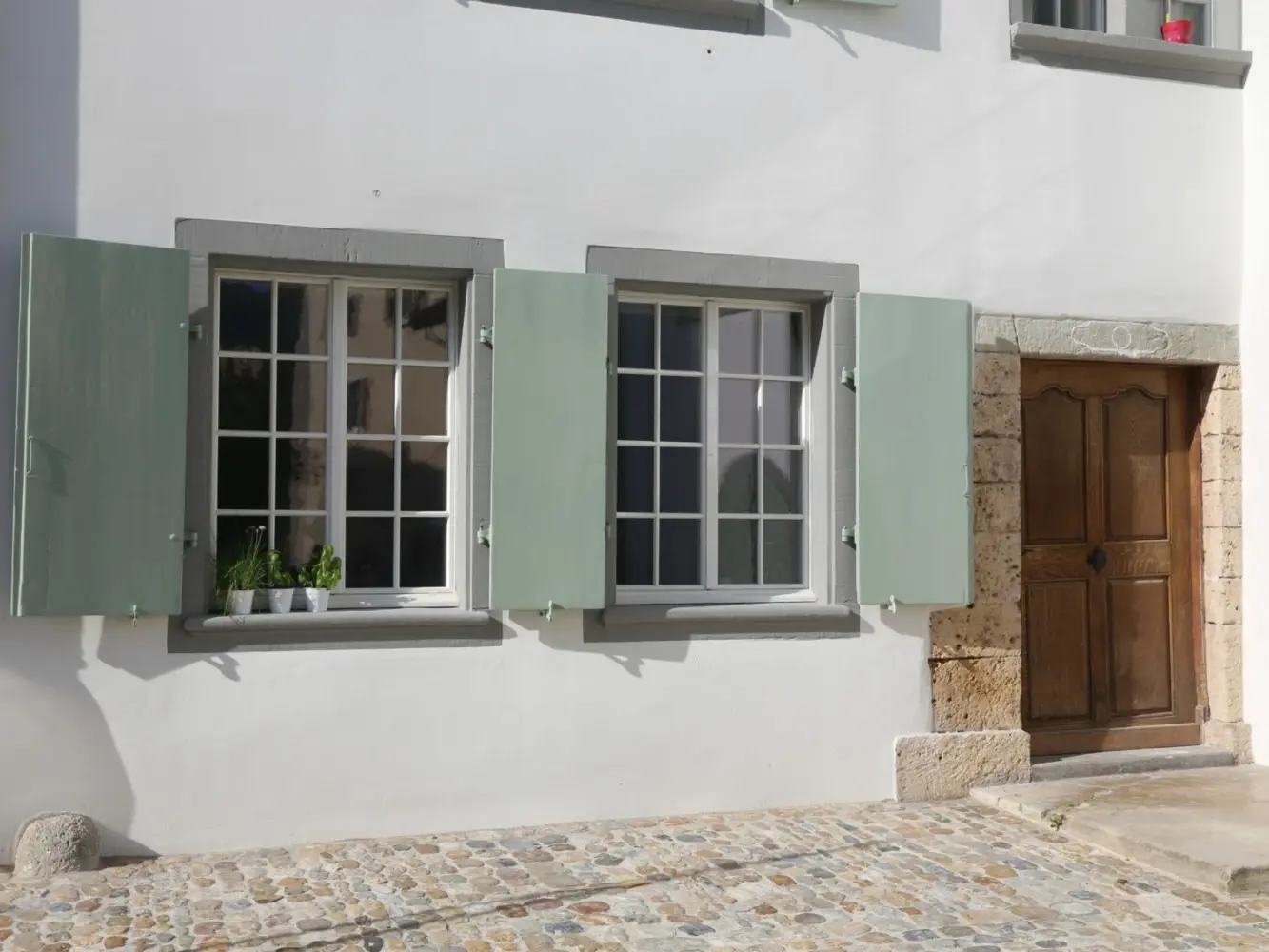Detailansicht des Eingangsbereichs mit Holztüre und zwei Fenstern mit grünen Fensterläden