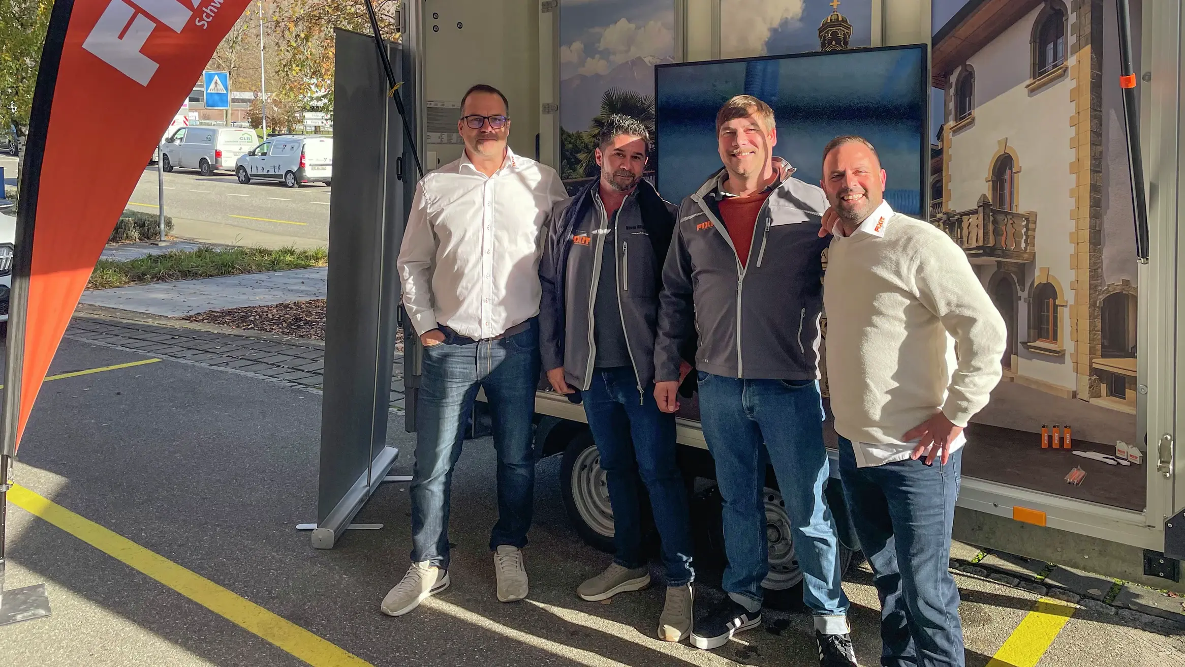 Samuel Blösch steht neben Kevin Maxwell, Michael Maron und Philipp Fellmann vor dem Roadshow Anhänger