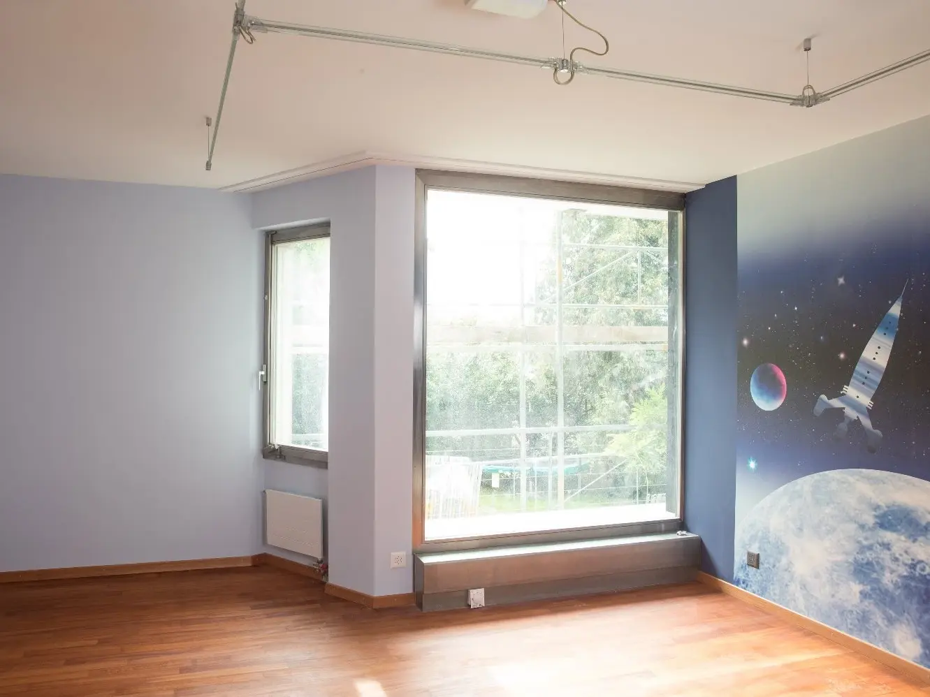 Murs enduits de bleu clair dans la chambre d'enfant, avec des fenêtres et un papier peint représentant la Terre et une navette spatiale