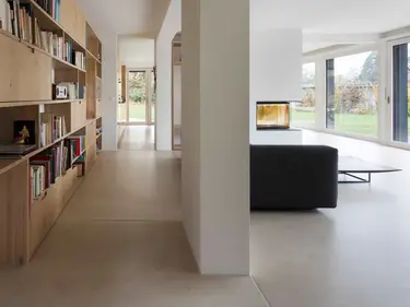 Salon moderne avec une grande étagère en bois pour les livres sur la gauche, un canapé noir, des murs et un plafond en plâtre.