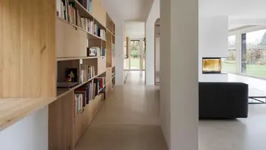 Moderner Wohnbereich mit grossem Holzregal für Bücher auf der linken Seite sowie Wänden und Decke mit Gipsputz