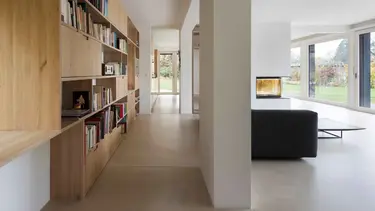 Salon moderne avec une grande étagère en bois pour les livres sur la gauche, un canapé noir, des murs et un plafond en plâtre.