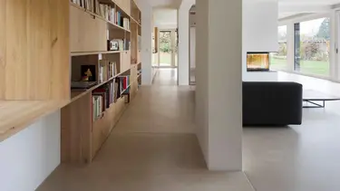 Moderner Wohnbereich mit grossem Holzregal für Bücher auf der linken Seite sowie Wänden und Decke mit Gipsputz