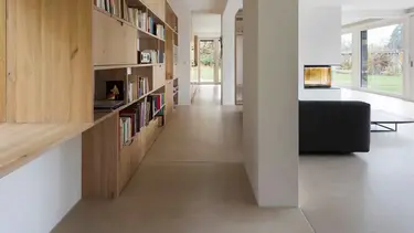 Moderner Wohnbereich mit grossem Holzregal für Bücher auf der linken Seite, einer Betonsäule und einem schwarzen Sofa sowie Wänden und Decke mit Gipsputz