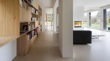 Moderner Wohnbereich mit grossem Holzregal für Bücher auf der linken Seite, einem schwarzen Sofa sowie Wänden und Decke mit Gipsputz