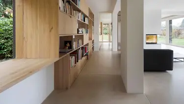 Moderner Wohnbereich mit grossem Holzregal für Bücher auf der linken Seite, einer Betonsäule und einem schwarzen Sofa sowie Wänden und Decke mit Gipsputz