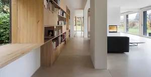 Moderner Wohnbereich mit grossem Holzregal für Bücher auf der linken Seite, einer Betonsäule und einem schwarzen Sofa sowie Wänden und Decke mit Gipsputz