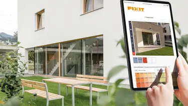 Rechts im Vordergrund sieht man ein Tablett mit dem Fixit Fassadenkonfigurator und den Händen des Nutzers, im Hintergrund ist ein modernes Einfamilienhaus