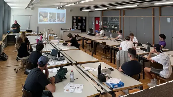Übersicht über den Schulungsraum am GIBZ mit den Schülern an zwei langen Tischreihen und Werner Wälle als Vortragender mit der Folien im Hintergrund