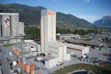 Vue aérienne de l'usine de production de Fixit AG à Untervaz avec la tour de production, les silos et l'entrepôt.