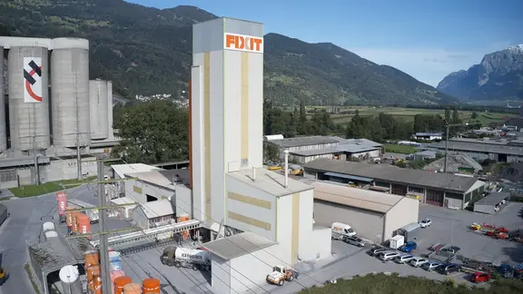 Vue aérienne de l'usine de production de Fixit AG à Untervaz avec la tour de production, les silos et l'entrepôt.