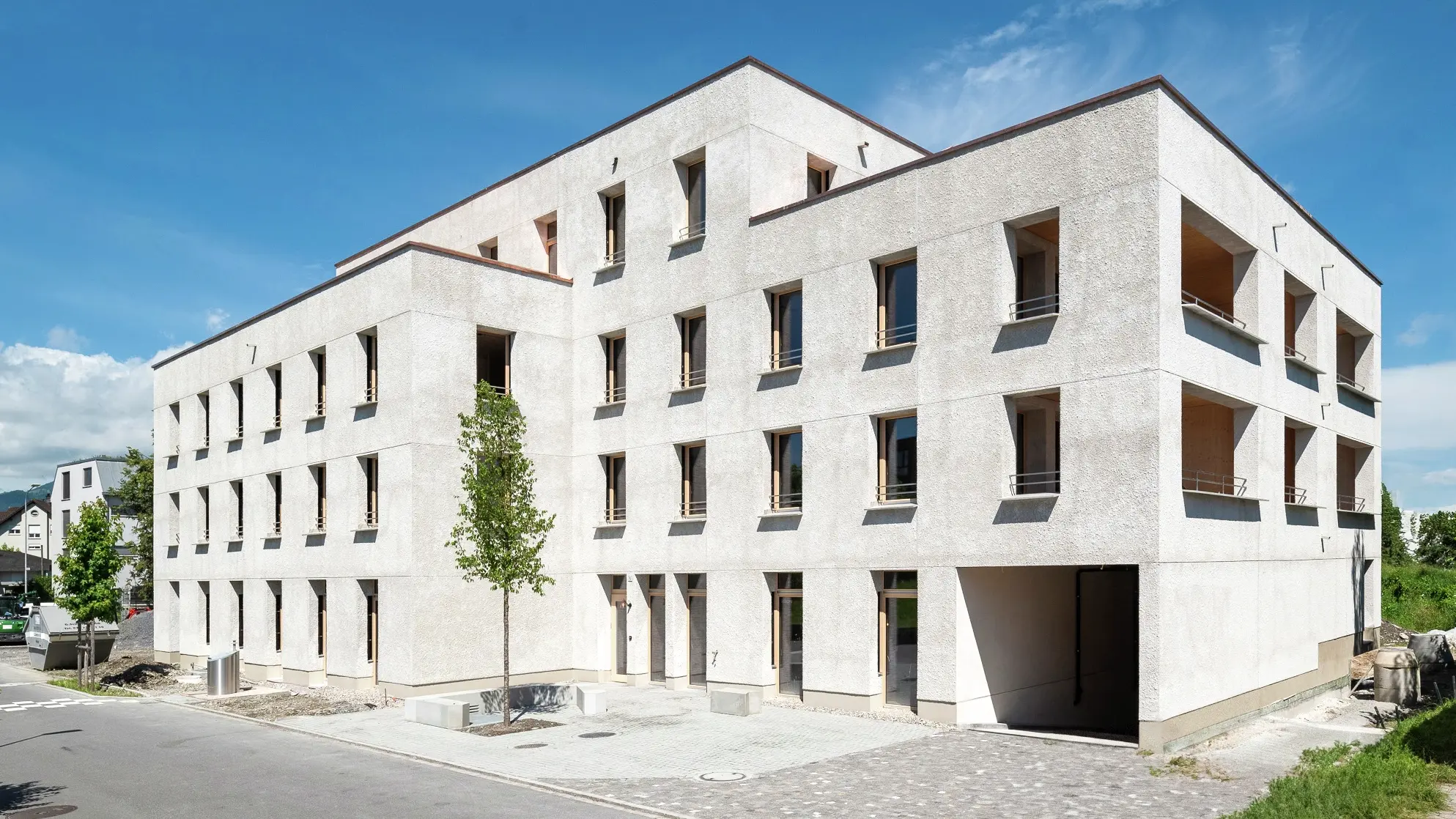 A modern, three-storey building clad in light-coloured natural stone, bathed in sunshine