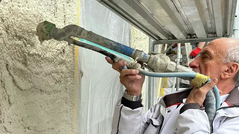 Vito Serratore applique l'enduit isolant CalceClima® sur un mur à l'aide d'une buse.