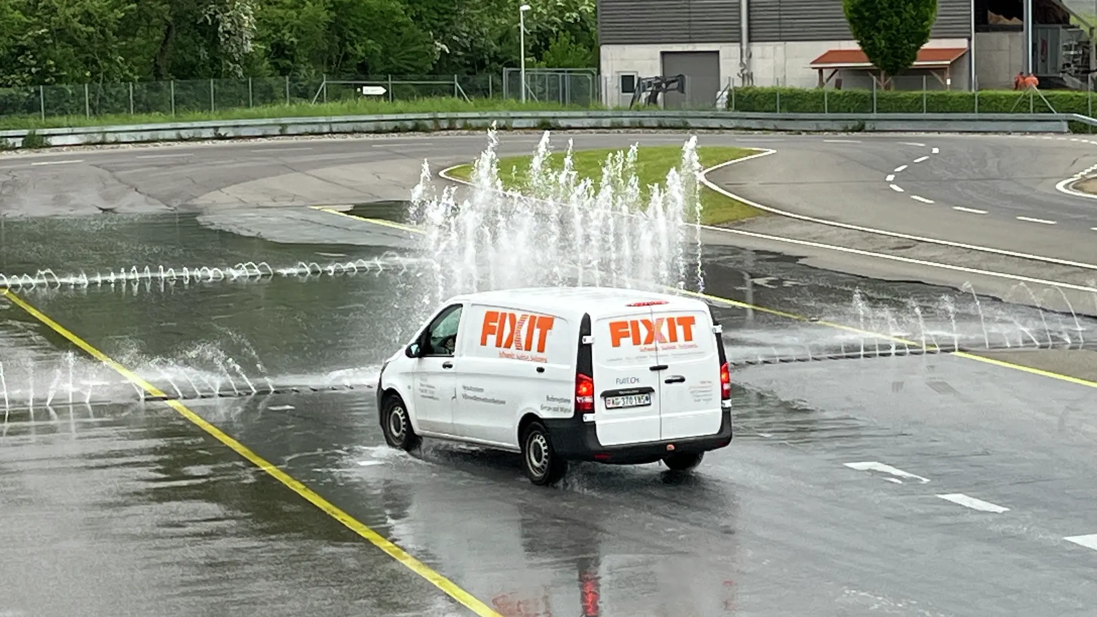 Ein weisser Van mit Fixit Beklebung absolviert die Aquaplaning-Strecke mit Wasserfontänen