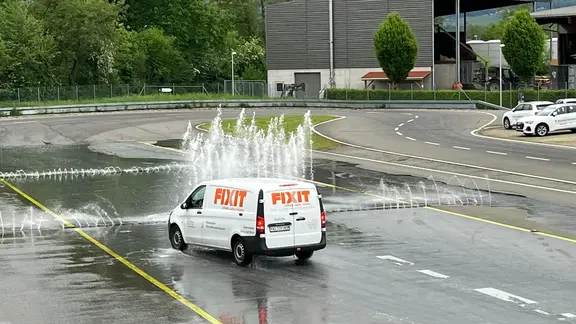 Ein weisser Van mit Fixit Beklebung absolviert die Aquaplaning-Strecke mit Wasserfontänen