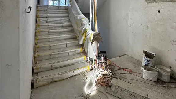 Historisches Treppenhaus im Rohzustand mit gewölbter Decke, Baustrahler und Fixit 163 Produkt Sack 