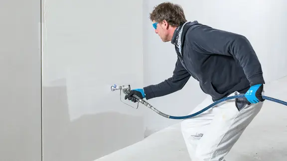 Die Spachtelmasse wird von einem Verarbeiter auf die Wand aufgespritzt.