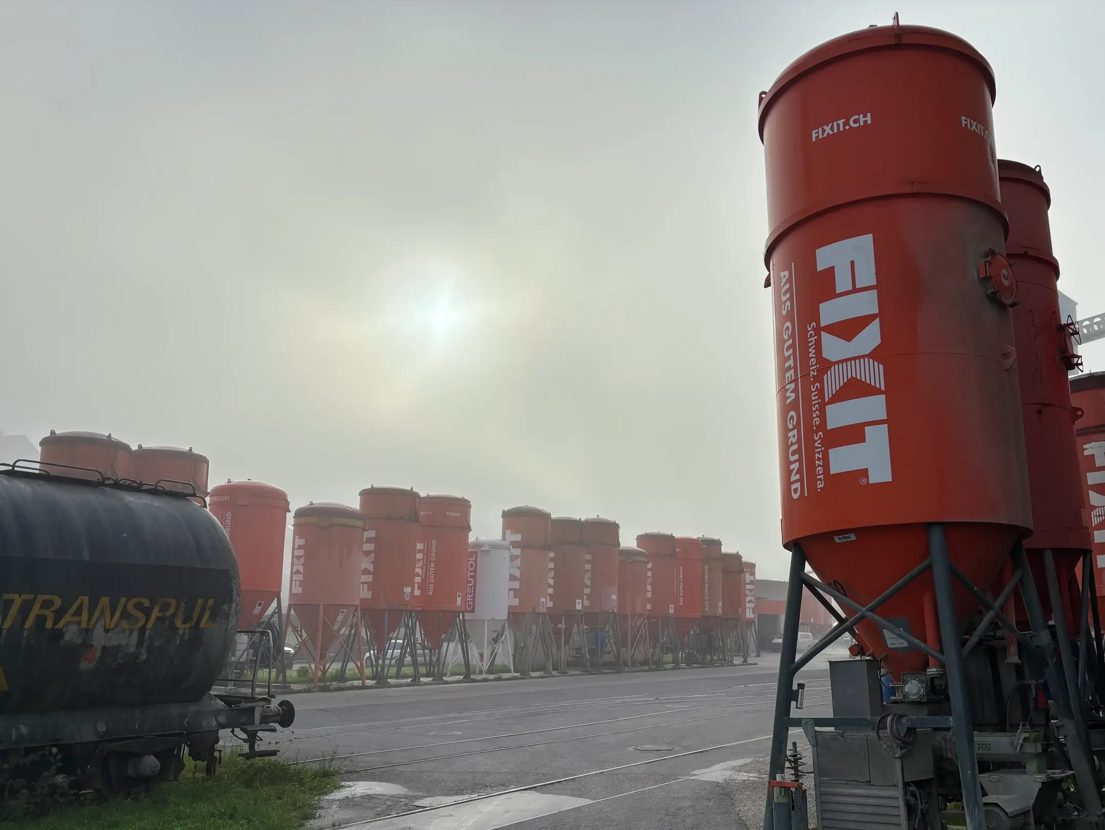 Orangenes Fixit Silo rechts im Vordergrund, weitere Silos in der Reihe im Hintergrund im Nebel mit Sonnenlicht