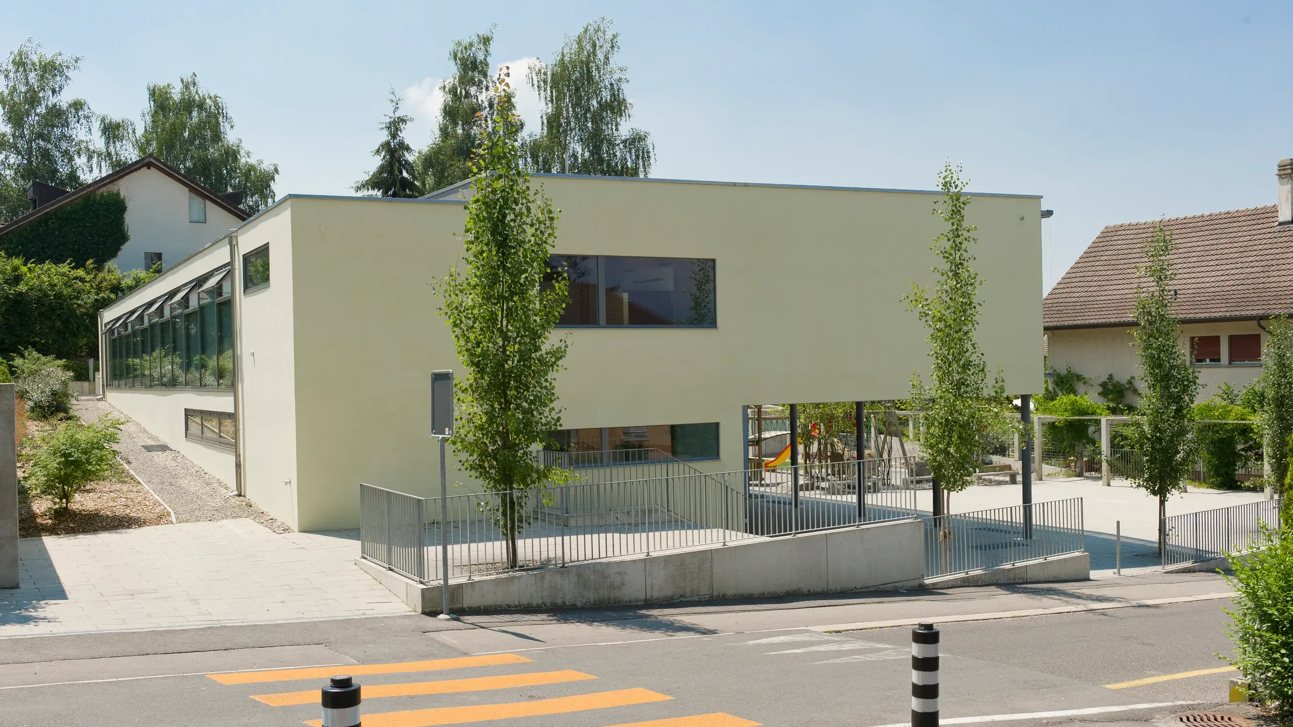 Bâtiment scolaire avec façade extérieure crépie en vert clair et quelques arbres