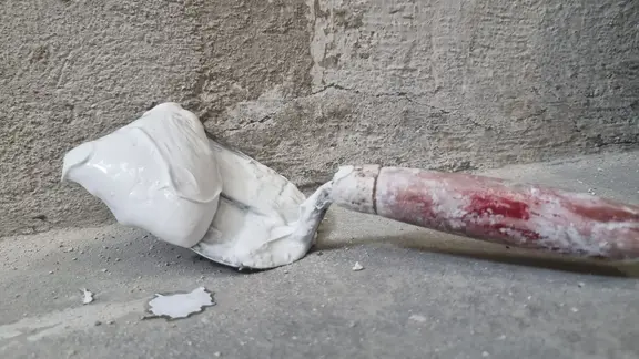 Kelle mit rotem Griff und Sumpfkalk darauf liegt auf dem Boden vor der zu verspachtelten Wand