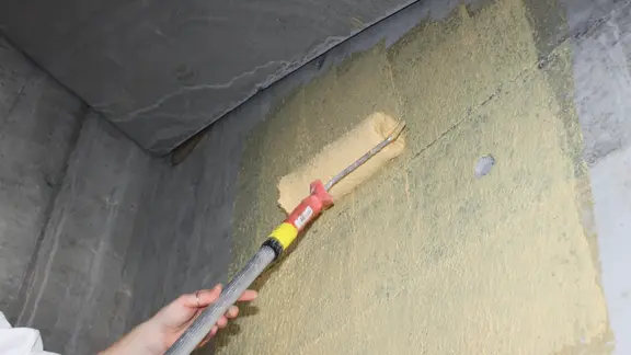 Die gelb eingefärbte Fixit 341 Combi Quarzhaftbrücke R+S wird mit der Rolle auf eine Betonwand appliziert