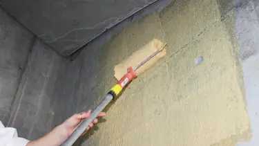Le pont d'adhérence en quartz Fixit 341 Combi R+S teinté en jaune est appliqué au rouleau sur un mur en béton.