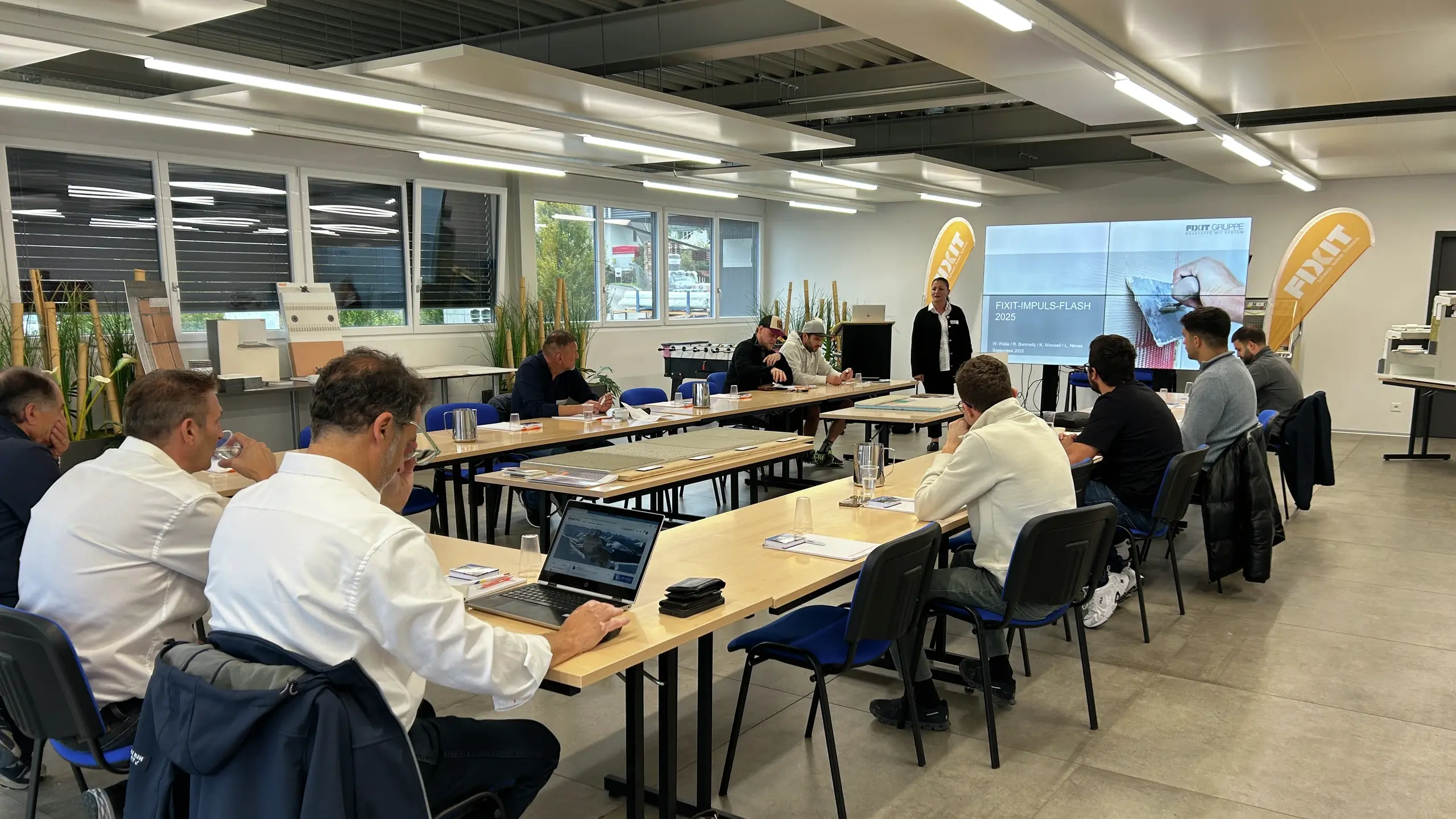 Ansicht über die Teilnehmenden an den Konferenztischen hin zu Rana Mehaidli, die die Teilnehmenden begrüsst