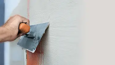 Une main munie d'une truelle métallique retire un enduit d'un mur