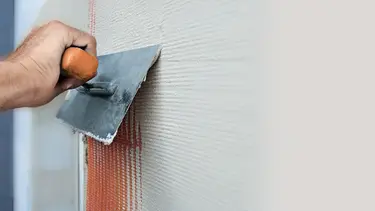 Une main munie d'une truelle métallique retire un enduit sur un treillis d'armature