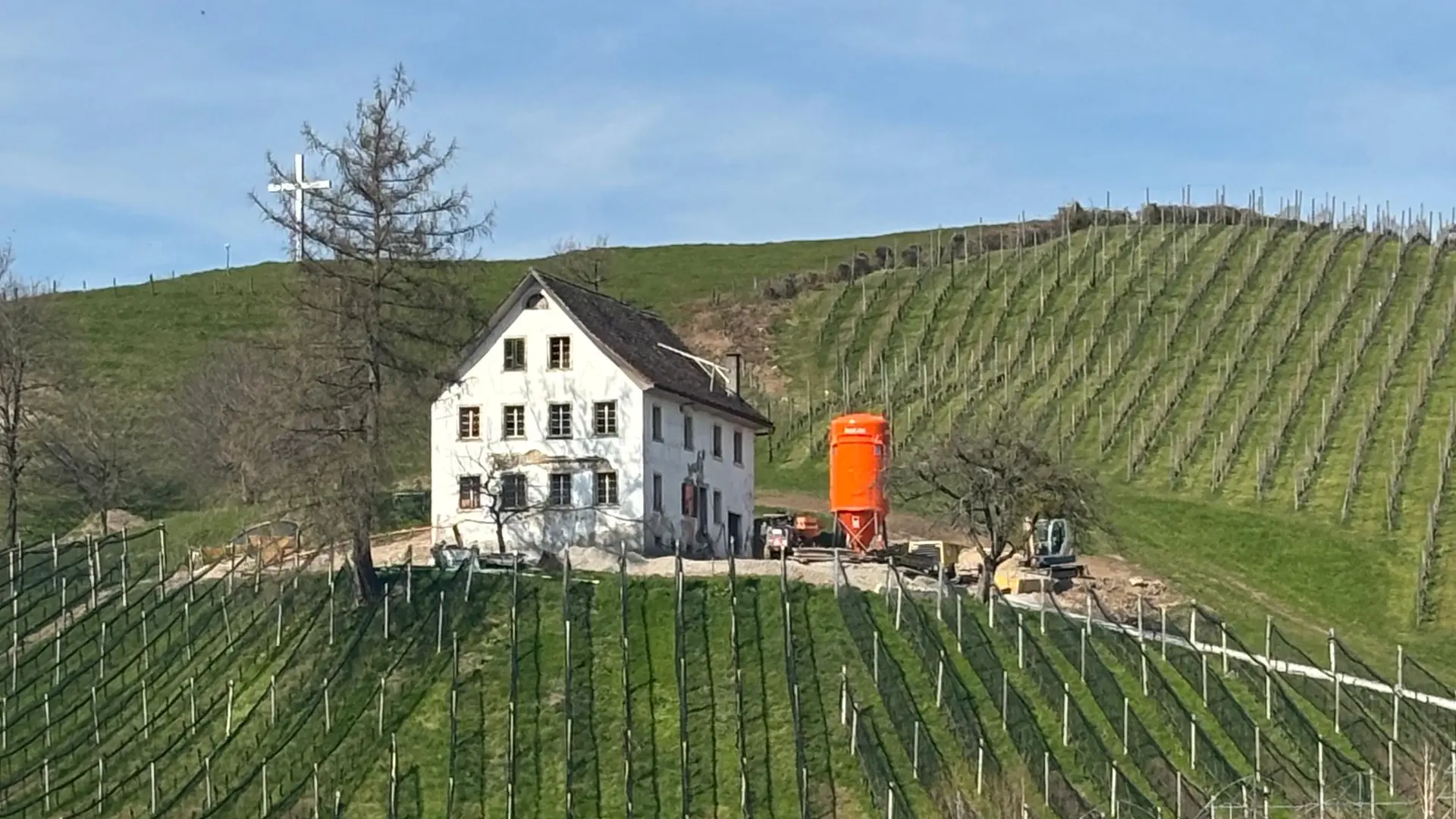 Dreistöckiges, weiss verputztes Haus bei schönem Wetter in den Weinbergen mit einem orangenen Fixit Silo