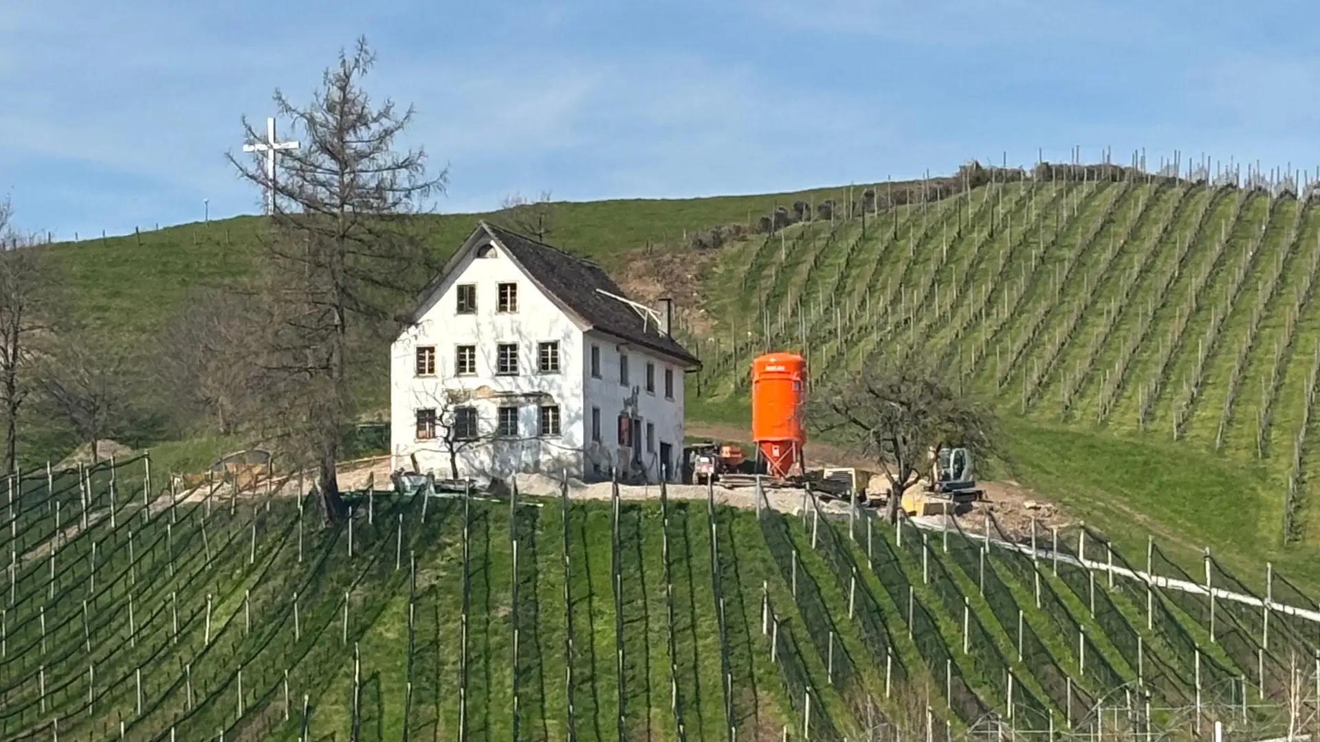 Dreistöckiges, weiss verputztes Haus bei schönem Wetter in den Weinbergen mit einem orangenen Fixit Silo