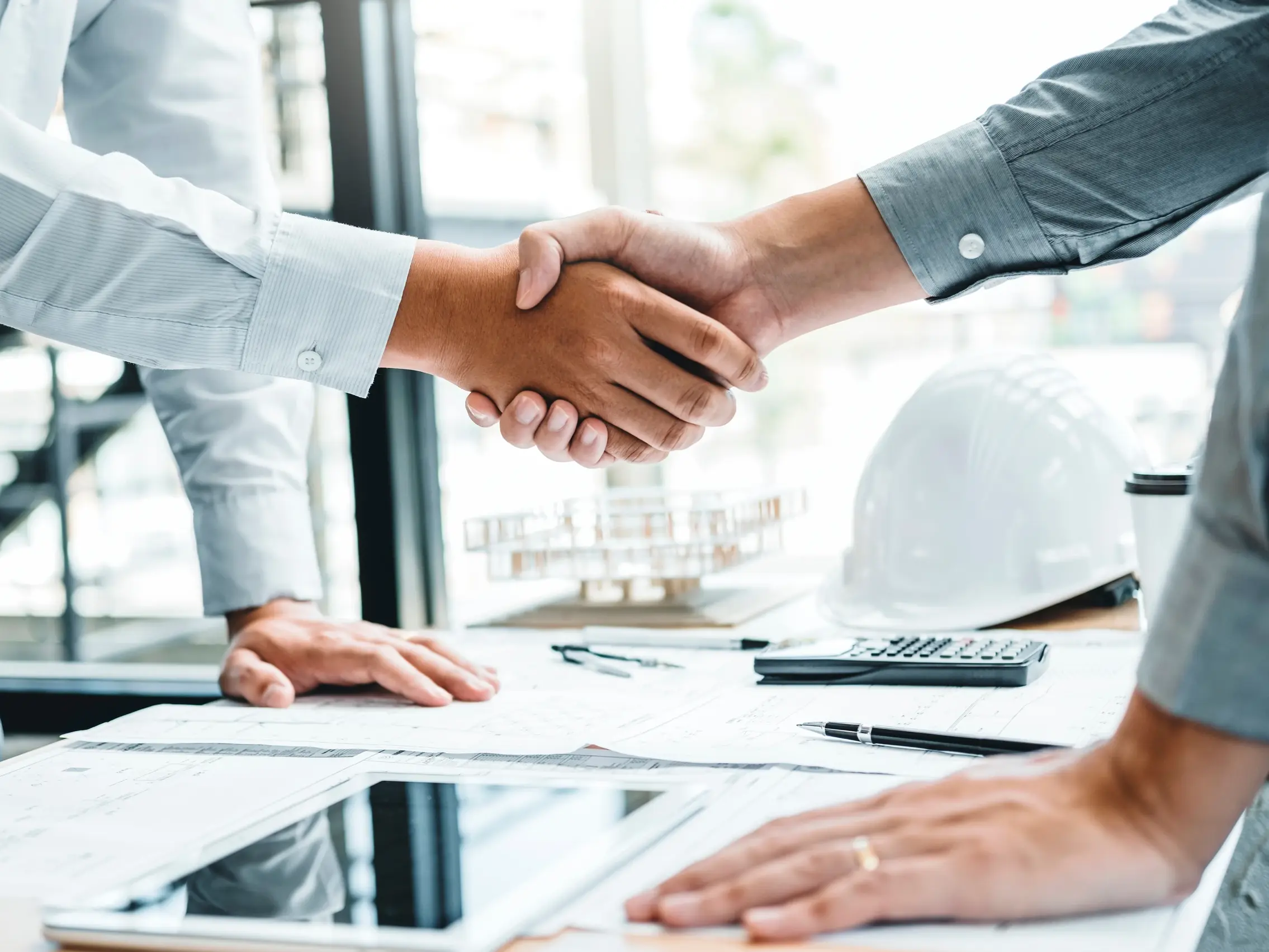 Due persone, una con una camicia bianca e l'altra con una grigio scuro, si stringono la mano davanti a una scrivania