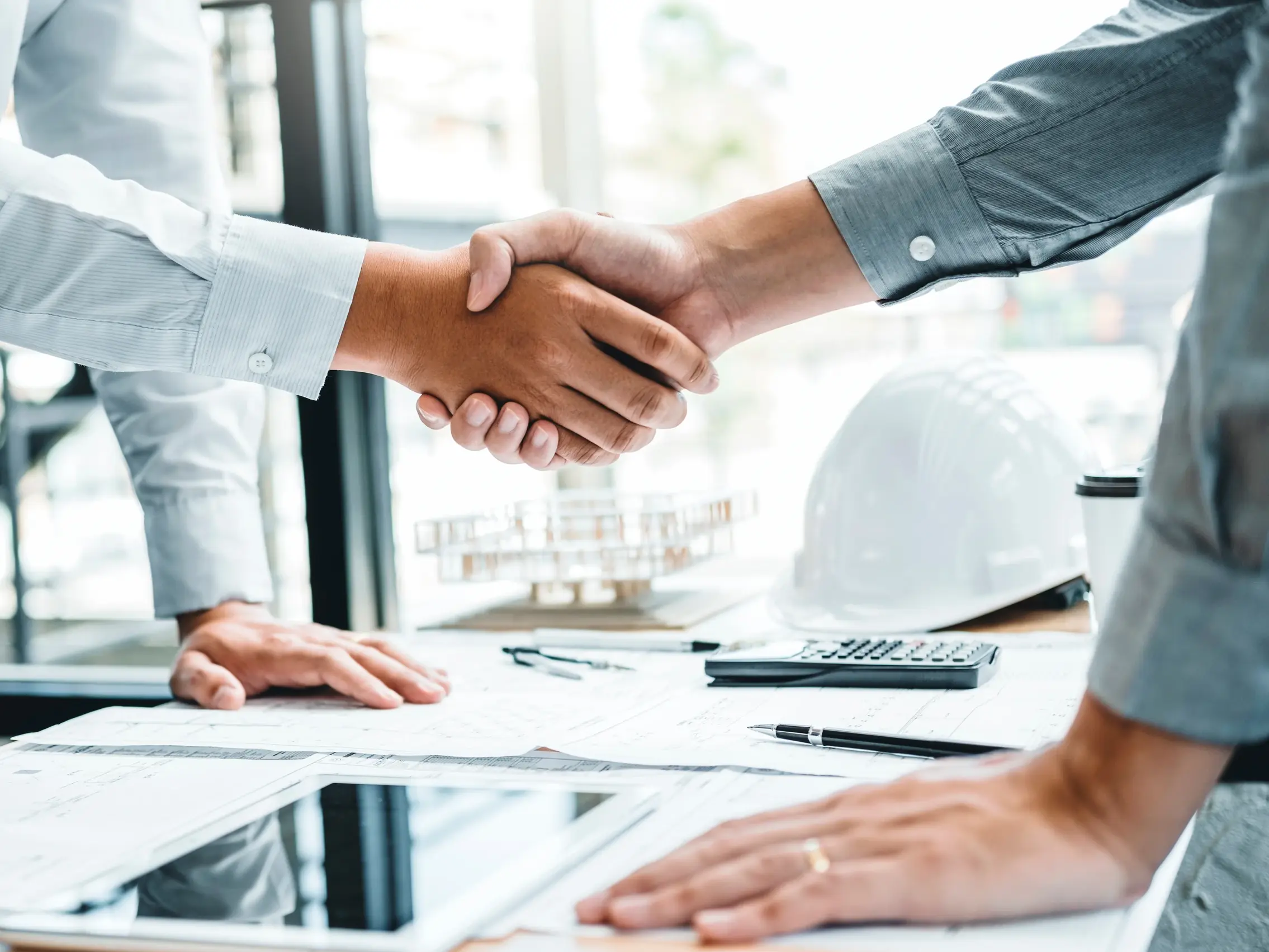 Due persone, una con una camicia bianca e l'altra con una grigio scuro, si stringono la mano davanti a una scrivania
