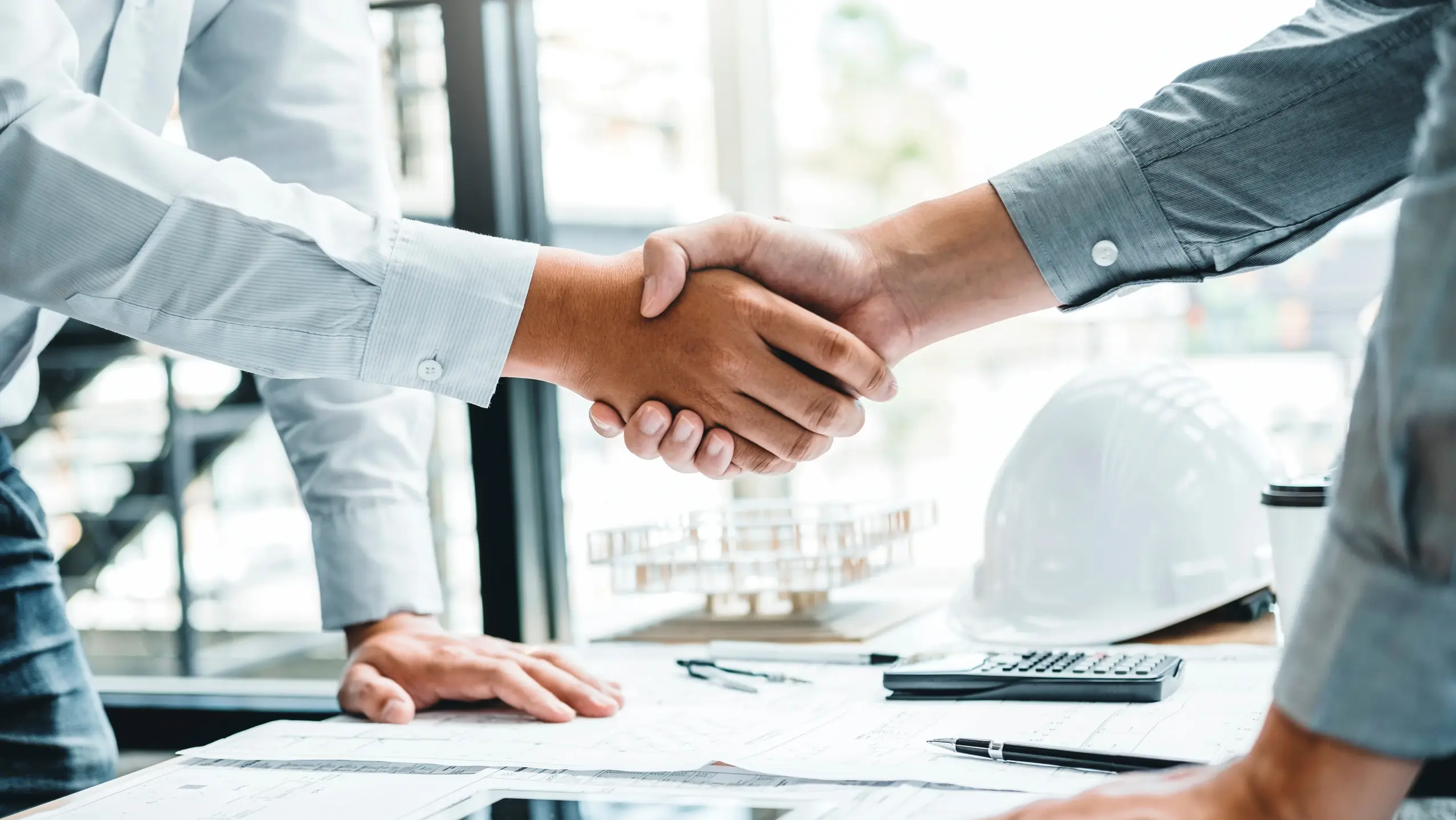  Due persone in camicia bianca e grigio scuro si stringono la mano sopra una scrivania