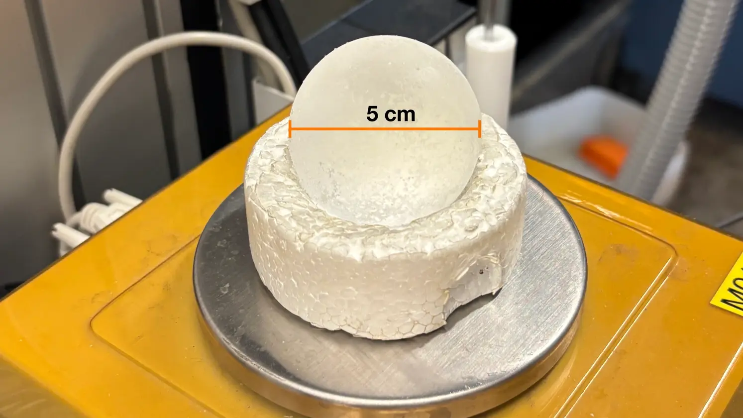 Un grêlon artificiel de 5 cm de diamètre (étiqueté) repose sur un moule en polystyrène posé sur une balance