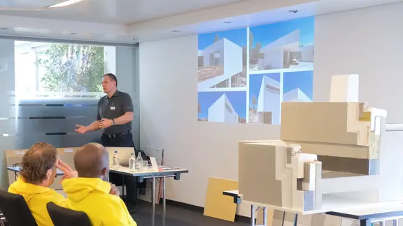 Ralf Bannwitz zeigt Bildbeispiele für Fixit RoofEtics® auf der Präsentation vor dem Publikum sowie das Ausführungsmuster rechts