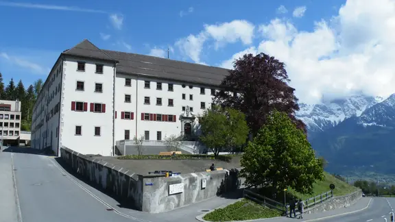 Bâtiment historique du couvent de Pfäfers avec façade extérieure en crépi blanc et volets rouges dans un panorama de montagne