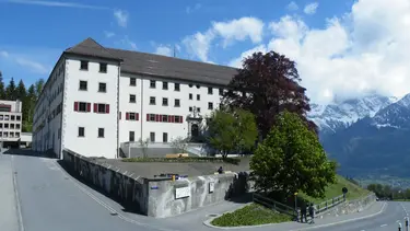 Bâtiment historique du couvent de Pfäfers avec façade extérieure en crépi blanc et volets rouges dans un panorama de montagne