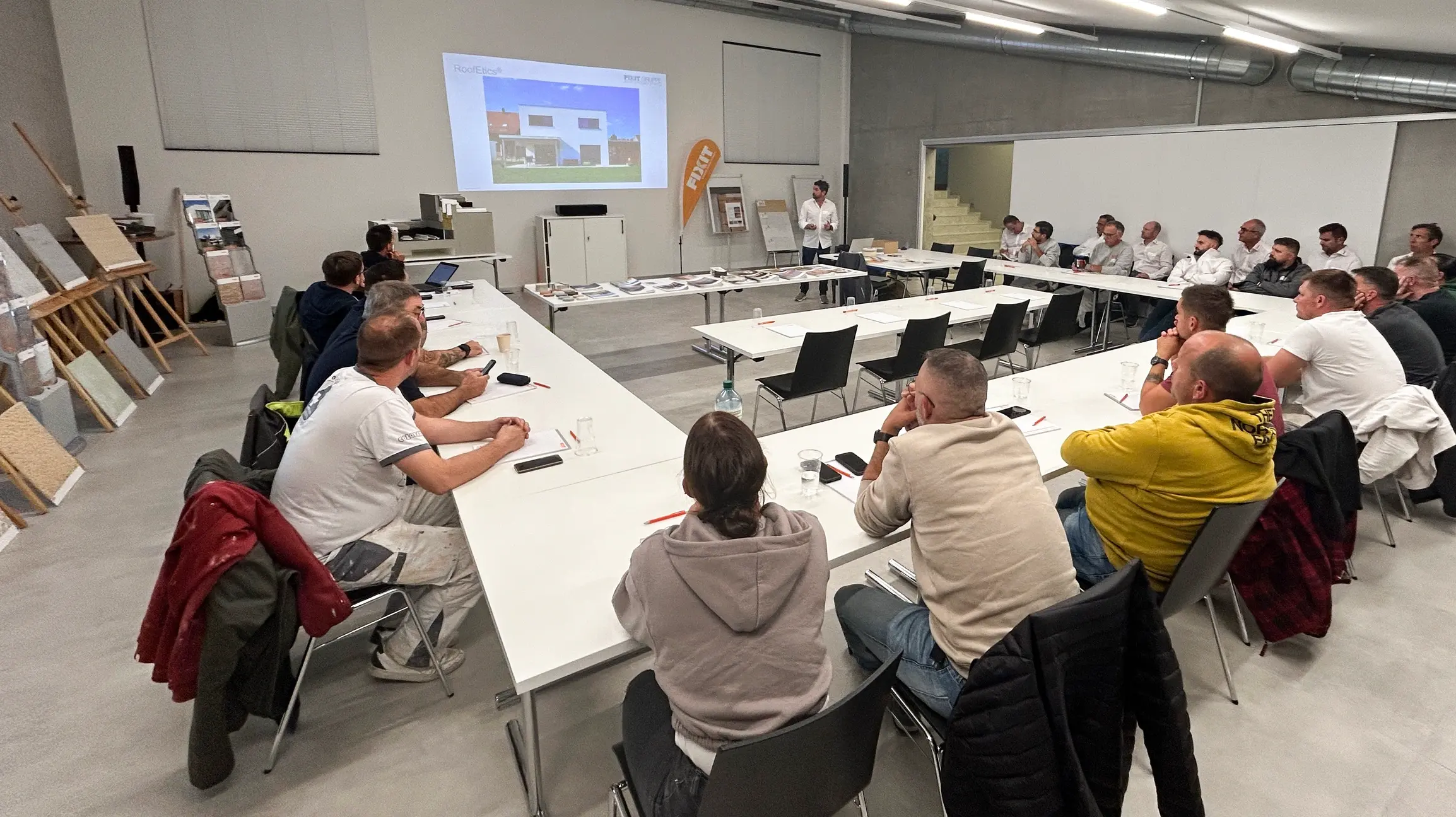 Les participants sont assis à des tables disposées en U et écoutent la conférence